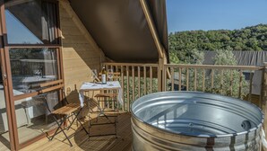 Une terrasse en bois avec une table et des chaises, un jacuzzi et une vue sur une colline boisée.