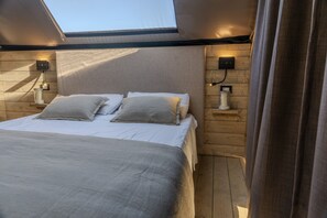 A bedroom with a bed, two bedside tables, a wall-mounted light, and a skylight.