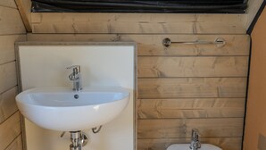 Une petite salle de bain avec un lavabo et un bidet blancs, des murs recouverts de panneaux en bois et un plafond en pente.