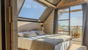 Une chambre avec une lucarne, un lit avec des oreillers, un plancher en bois et une vue sur l’extérieur.