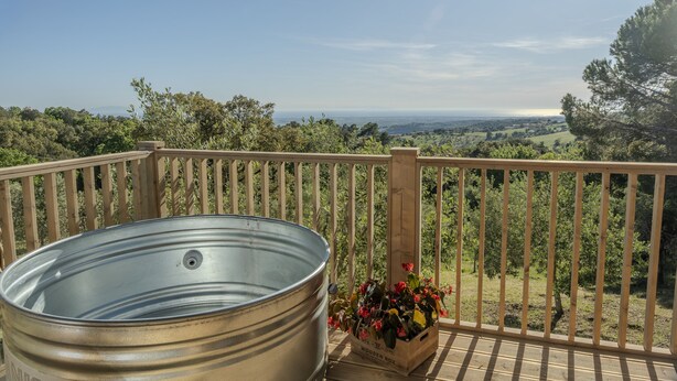 Un bain à remous en métal installé sur une terrasse en bois, offrant une vue sur le paysage.