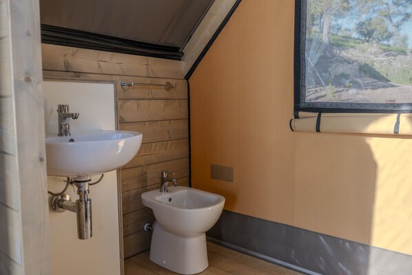 A bathroom with a white sink, a bidet, and a window with a view of trees.