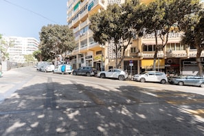 A street with parked cars, a police van, and commercial buildings with shops. - MalagaSuite Urban Beach D (Torremolinos)