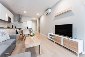 A modern living room with a flat-screen TV, a sofa, a dining table, and a kitchen area in the background. - MalagaSuite Urban Beach D (Torremolinos)