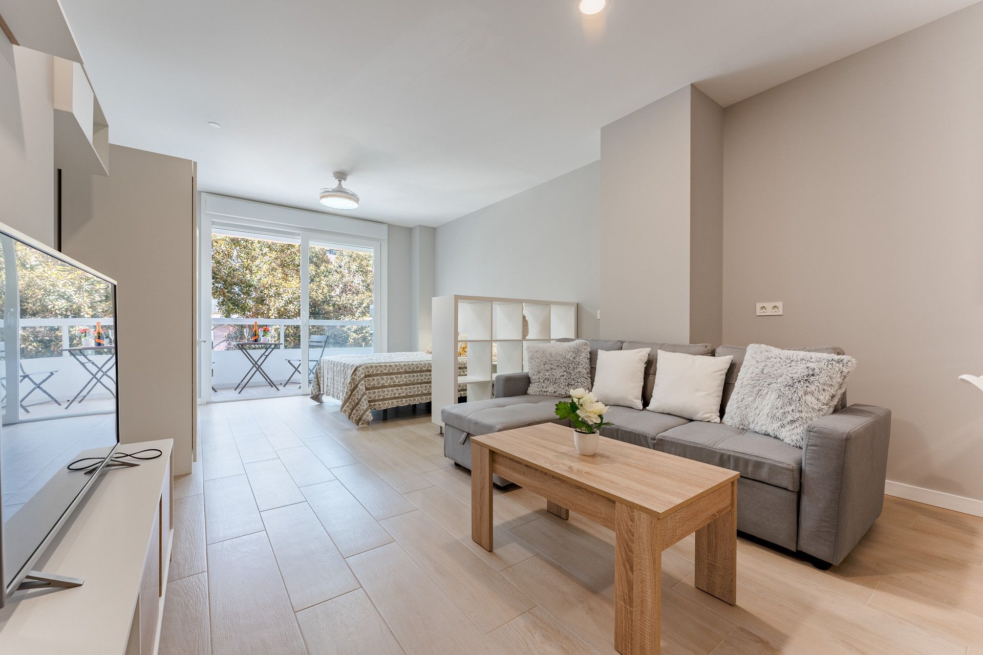 A spacious living room with a grey sofa, a wooden coffee table, and a balcony with a table and chairs.