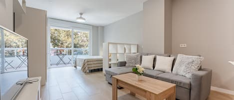 A spacious living room with a grey sofa, a wooden coffee table, and a balcony with a table and chairs.