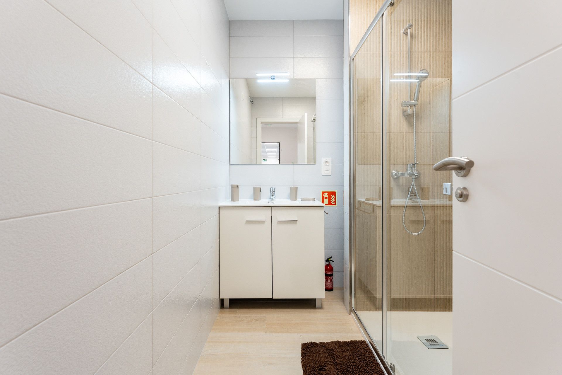 Un baño moderno con cabina de ducha de vidrio, paredes con azulejos blancos y suelo de madera.