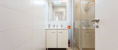 Un baño moderno con cabina de ducha de vidrio, paredes con azulejos blancos y suelo de madera.