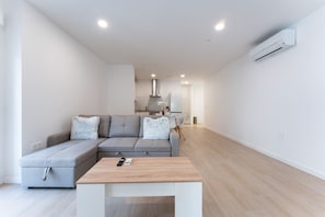 A modern living room with a grey sectional sofa, a wooden coffee table, and a kitchen in the background. - MalagaSuite Urban Beach E (Torremolinos)