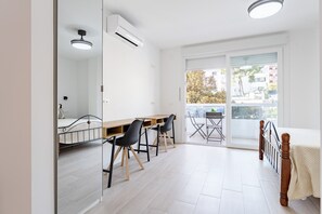 A modern room with a bed, a desk, and chairs, a window with a view of buildings, and an air conditioning unit. - MalagaSuite Urban Beach E (Torremolinos)