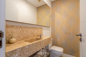 A bathroom with a marble countertop, two sinks, a toilet, and a wooden door with vertical lines. - Apt. w/ Jacuzzi in Condo. w/ Pool Cmn0304 (Florianópolis)