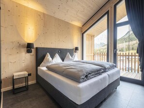 A bedroom with a bed, two wall-mounted lamps, a small bedside table, and a view of a balcony with a wooden railing. - Chalet With 4 Bedrooms & Sauna (Biberwier)