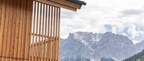 A wooden structure with vertical slats, a mountain range in the background, and a forested valley.