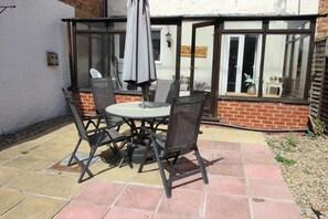 An outdoor patio with a round table and four chairs, a window with a view of the interior, and a brick wall. - The Hampton (Scarborough)