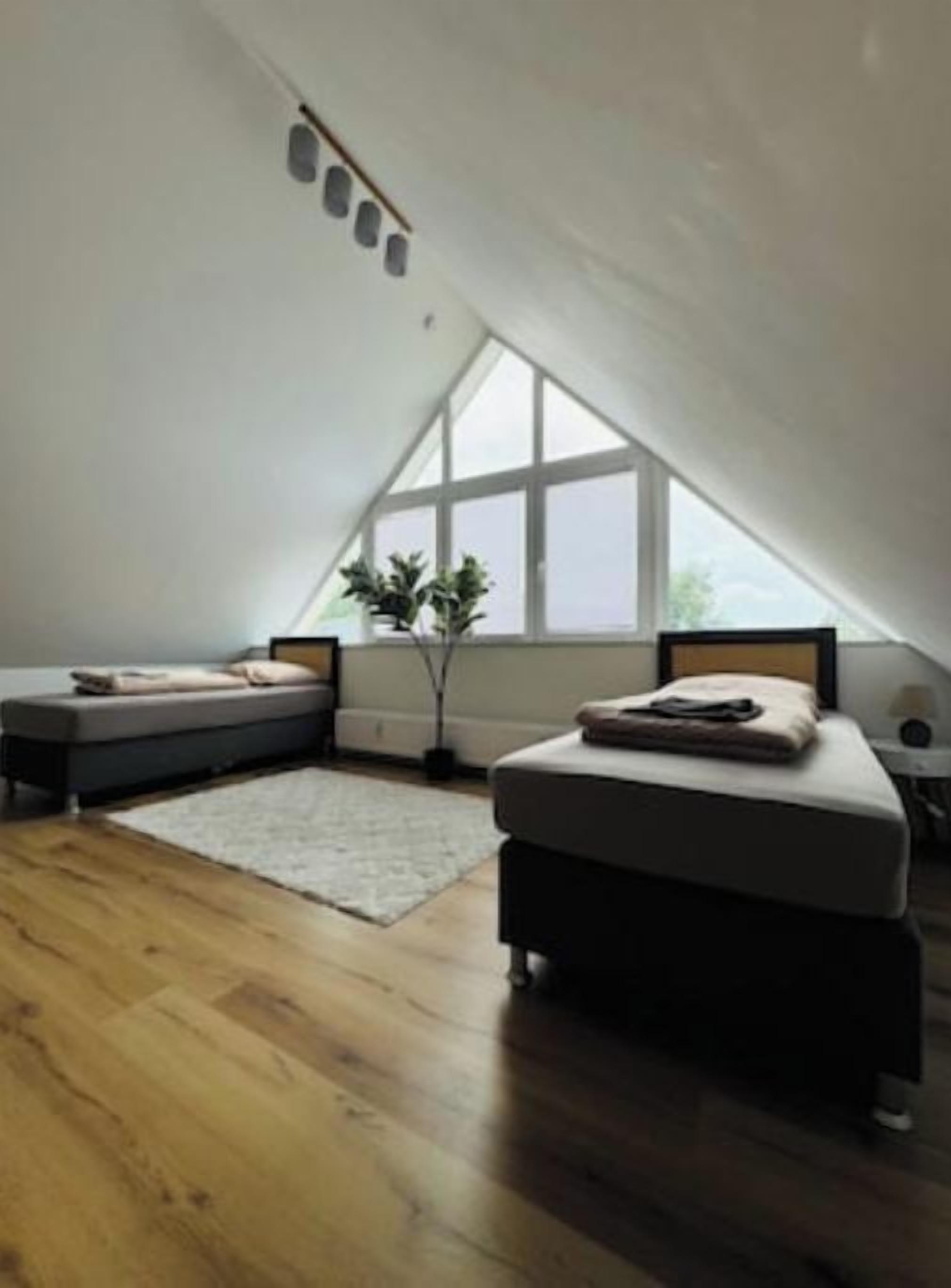 A bedroom with a sloped ceiling, a large window, a bed, a bedside table, and a small seating area.