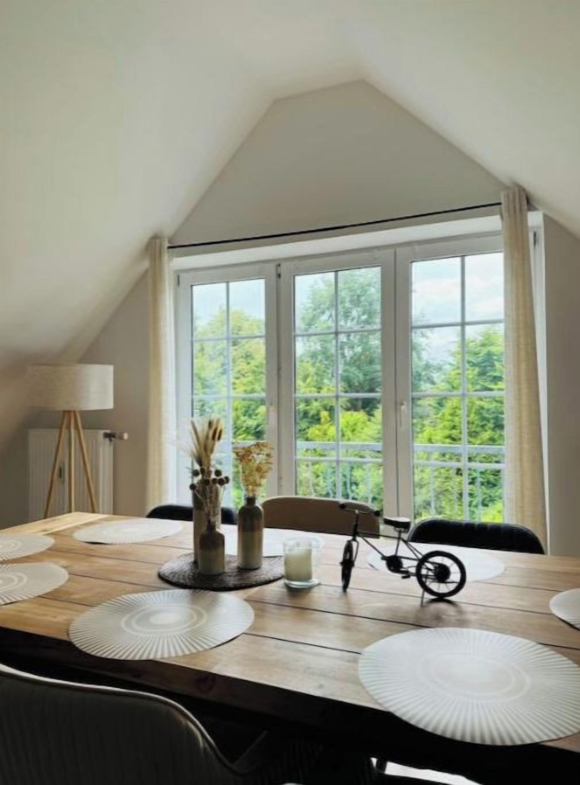 A dining area with a table set for four, large windows, and a view of greenery outside.