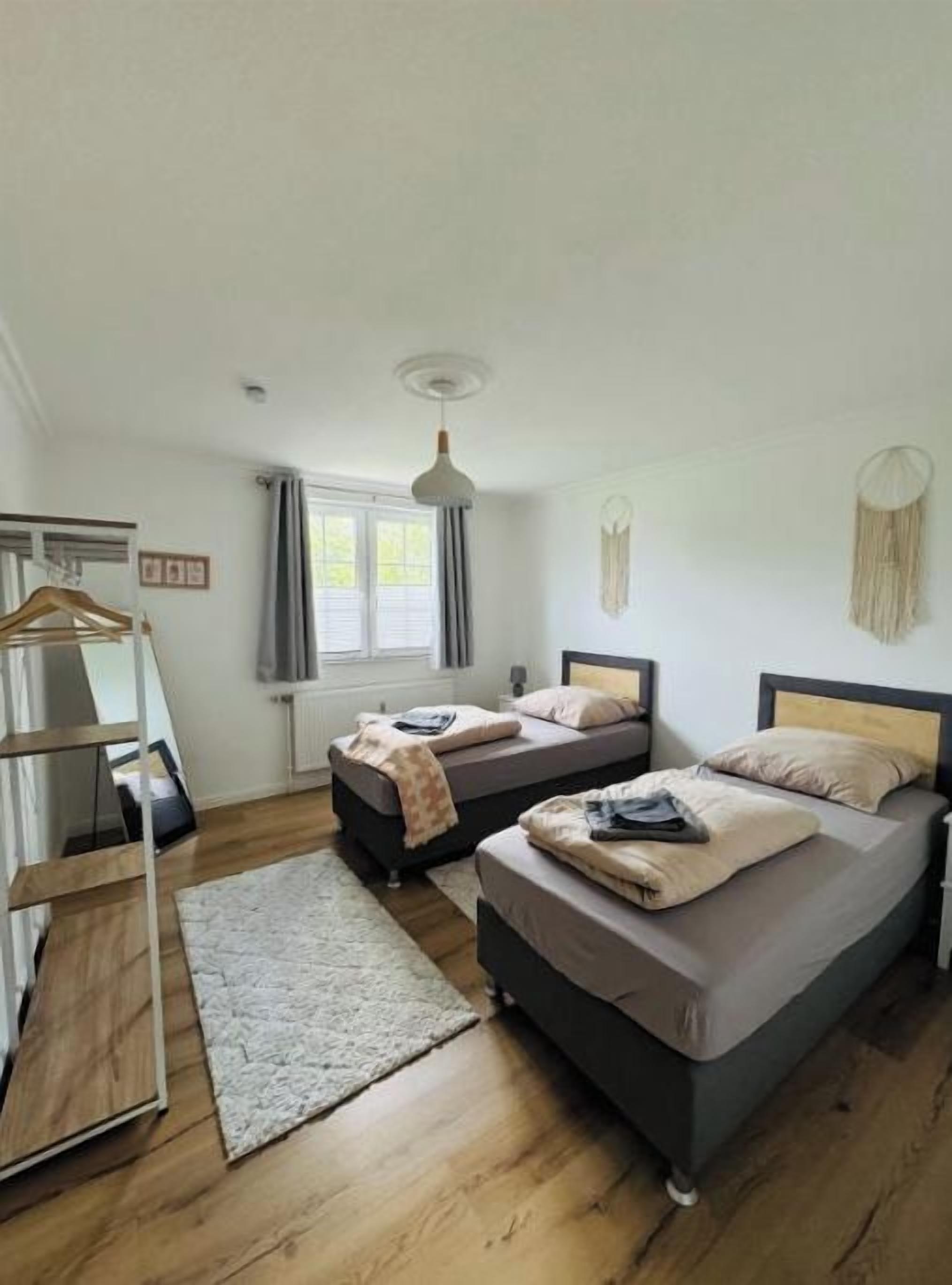 Een slaapkamer met twee bedden, een houten vloer, een hanglamp en een raam met gordijnen.