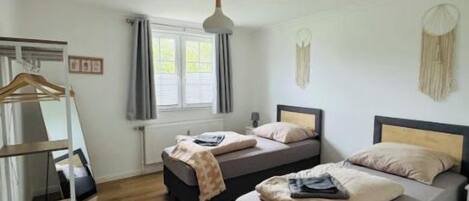 Een slaapkamer met twee bedden, een houten vloer, een hanglamp en een raam met gordijnen.