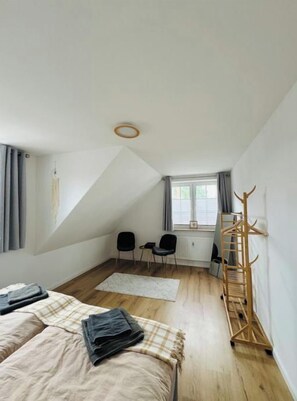 A modern bedroom with a sloped ceiling, a bed with a plaid bedspread, a wooden drying rack, and a small seating area with chairs. - Family Home by the Sea | 125 m² | Beach | Parking (Scharbeutz)