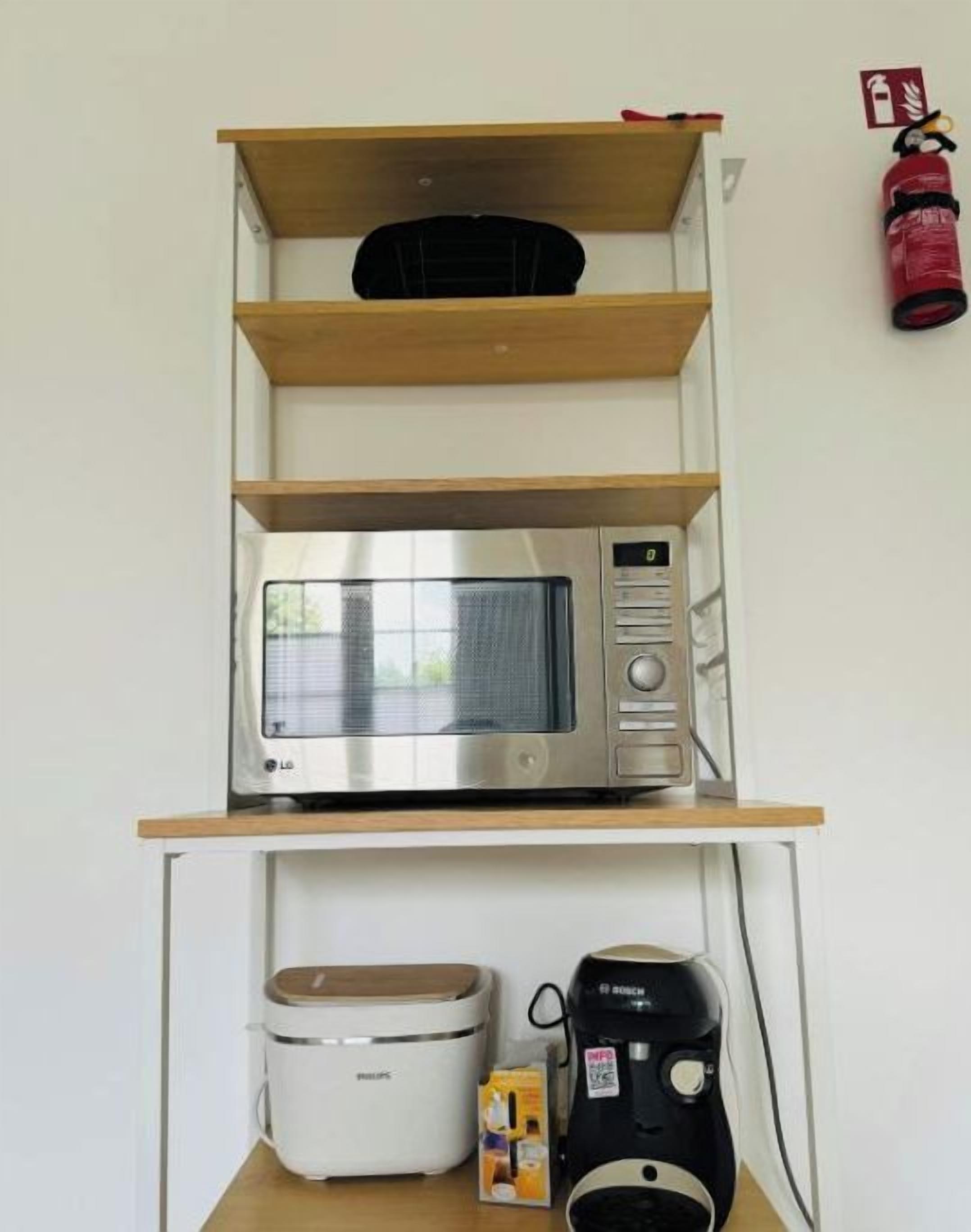 Une petite cuisine équipée d’un four à micro-ondes, d’un grille-pain et d’une machine à café, le tout posé sur une étagère en bois.