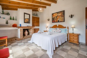 A bedroom with a bed, bedside tables, a fireplace, and a painting on the wall. - Villa Tarongers - By Dream Villas Pollensa (Pollensa)
