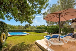 A swimming pool with a surrounding garden, a lounge area with chairs and an umbrella, and a clear sky. - Villa Tarongers - By Dream Villas Pollensa (Pollensa)