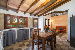 A kitchen with a wooden table, chairs, and a dining area with a sofa and a refrigerator. - Villa Tarongers - By Dream Villas Pollensa (Pollensa)