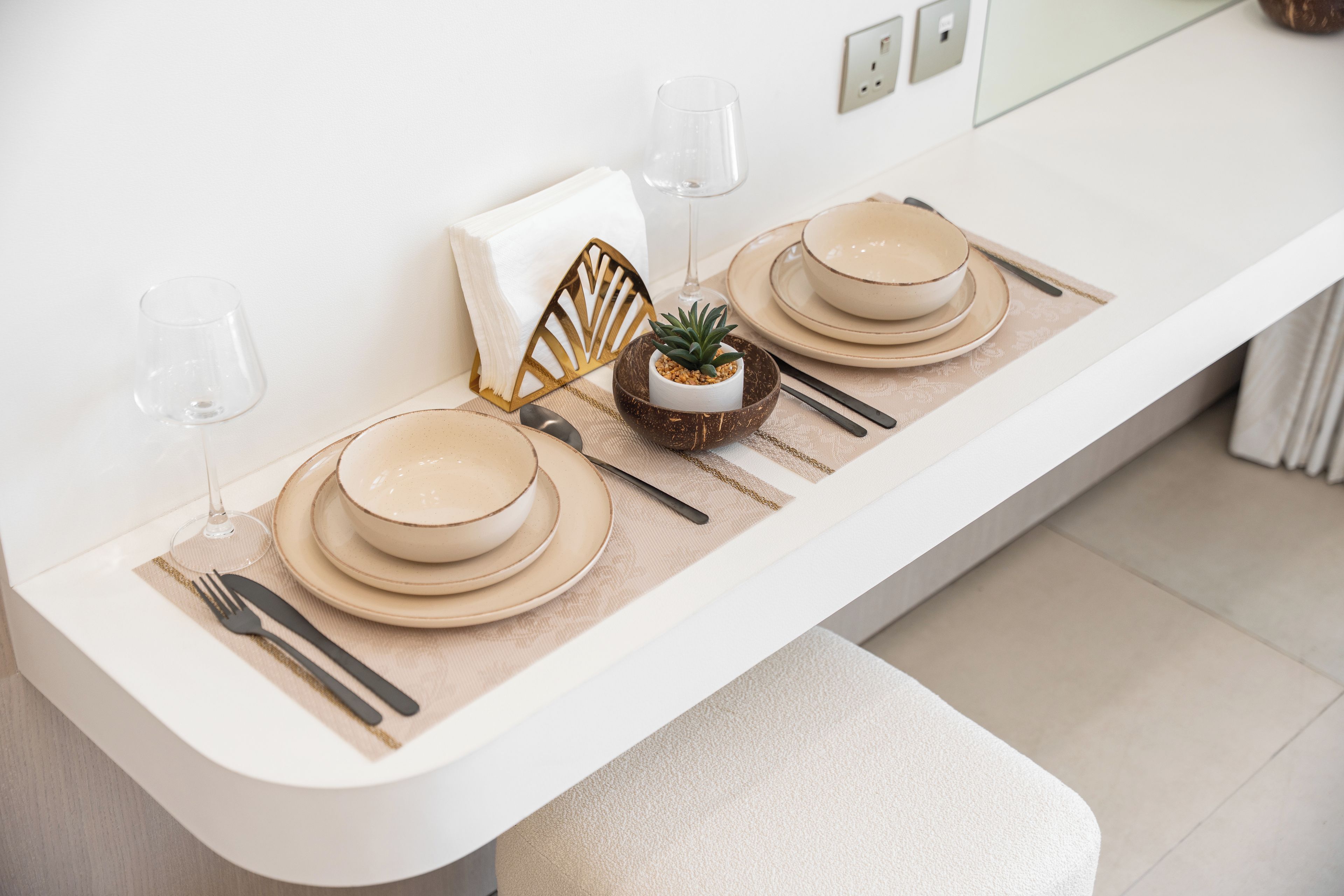 Une table à manger élégamment dressée, avec des assiettes, des couverts et des verres, un petit arrangement floral en guise de centre de table et un objet décoratif doré.
