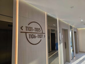 A hotel corridor with directional signs indicating room numbers 1101-1105 and 1106-1107. - Luxury Top-Floor Studio in JVC with Panoramic Terrace (JVC)