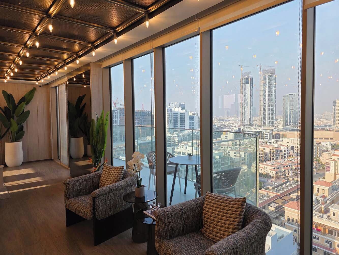 A high-rise interior with large windows, two sofas, a small table, and potted plants.