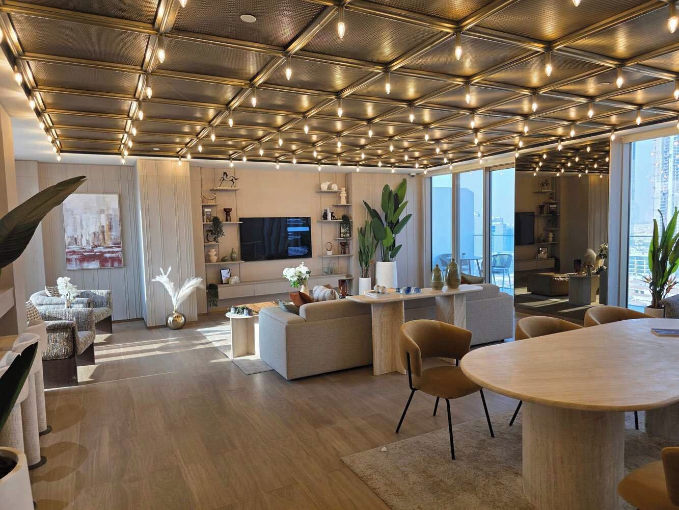 A spacious living area with a modern design, featuring a large sofa, a dining table, and a kitchen in the background.