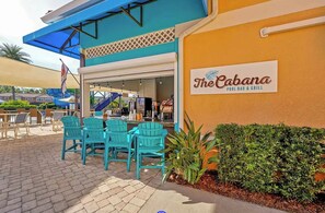 Zona d'estar a l'aire lliure amb cadires i taules turquesa, un bar de piscina i un rètol de 'The Cabana Pool Bar & Grill'.