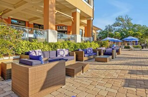 An outdoor seating area with wicker furniture and cushions, a sports bar and grill, and a Clubhouse sign. - 4BR townhouse at Regal Oaks (Kissimmee)