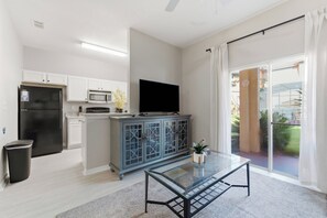 A modern kitchen with white cabinets, a black refrigerator, a microwave, and a stove. There's a glass table with a plant, and a sliding glass door leading to a balcony. - 4BR townhouse at Regal Oaks (Kissimmee)