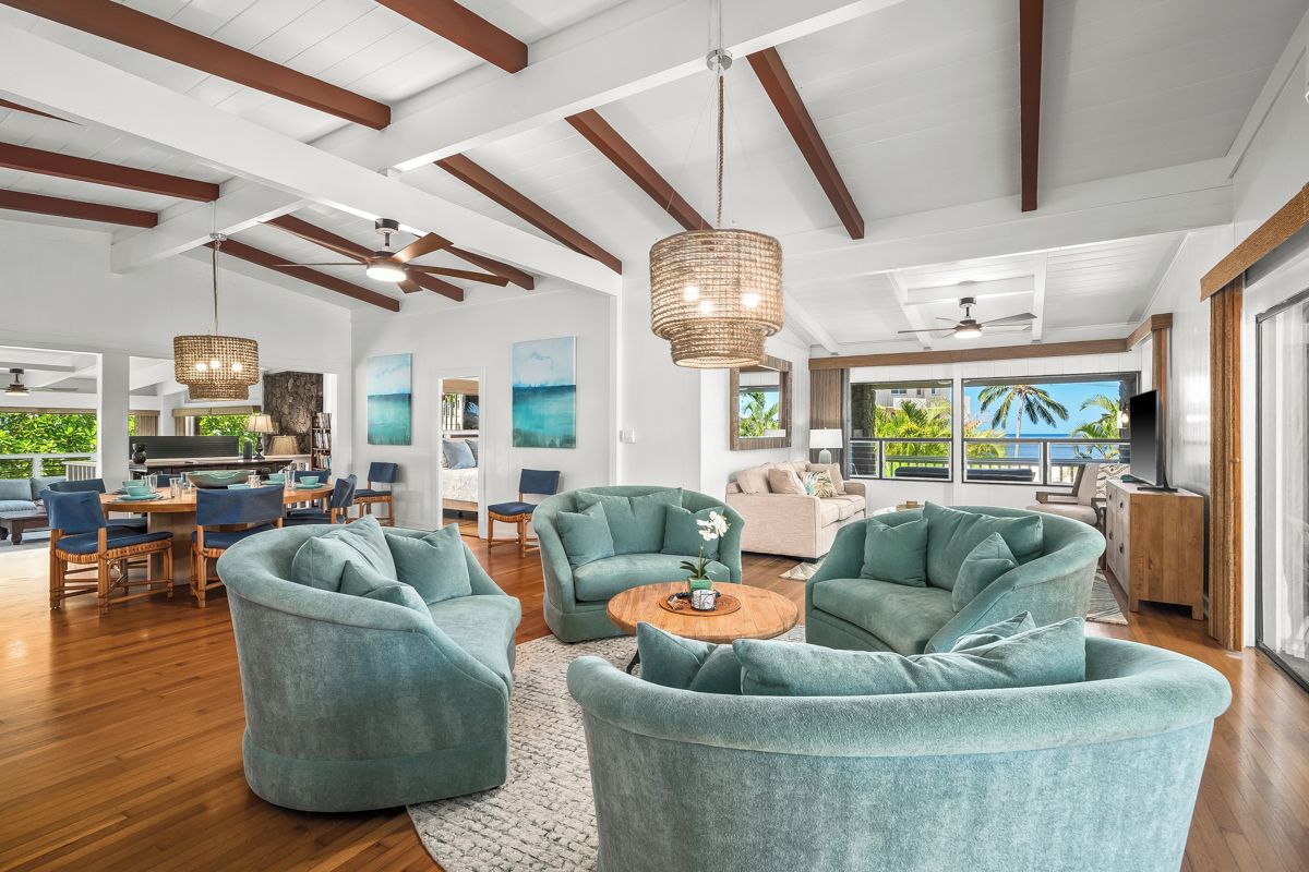 A spacious living area with teal armchairs, a wooden coffee table, and a large window offering a view of the outdoors.