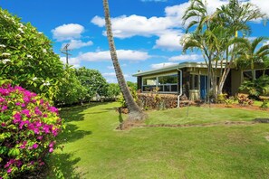A house with a well-maintained lawn, palm trees, and a clear sky. - Private Poipu Retreat with Rooftop Ocean Views, Hot Tub and Outdoor Living (Koloa)