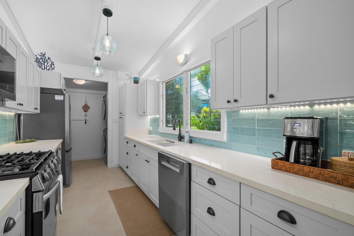 Una cocina moderna con armarios blancos, estufa a gas, lavavajillas y cafetera.