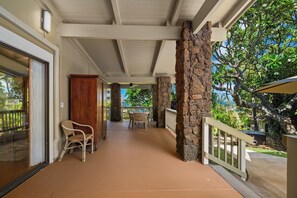 A covered outdoor area with a stone pillar, a wicker chair, and a table. - Private Poipu Retreat with Rooftop Ocean Views, Hot Tub and Outdoor Living (Koloa)