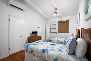 A bedroom with two beds, a ceiling fan, a TV on a wooden stand, and a door. - Private Poipu Retreat with Rooftop Ocean Views, Hot Tub and Outdoor Living (Koloa)
