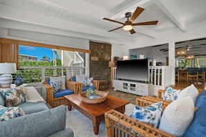 A spacious living area with a ceiling fan, a stone wall, a flat-screen TV, and wicker furniture. - Private Poipu Retreat with Rooftop Ocean Views, Hot Tub and Outdoor Living (Koloa)