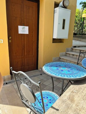 A wooden door with a sign, a white electrical box, outdoor stairs, and a tiled table with a metal chair. - Verde Salvia Home - Vacation Rental in Frascati (Frascati)