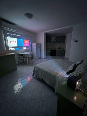 A modern hotel room with a bed, a desk, a chair, a TV displaying streaming services, and a kitchenette. - Verde Salvia Home - Vacation Rental in Frascati (Frascati)