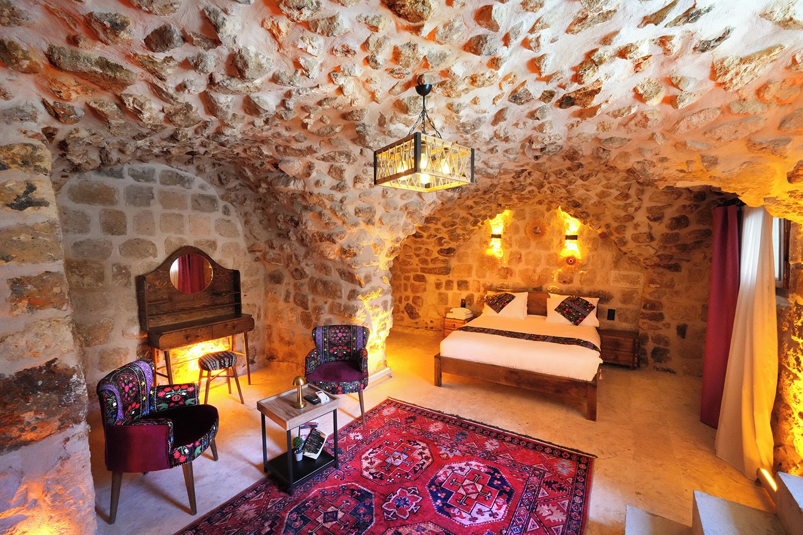 A cozy room with a stone wall, a bed, a wooden piano, and a patterned rug.
