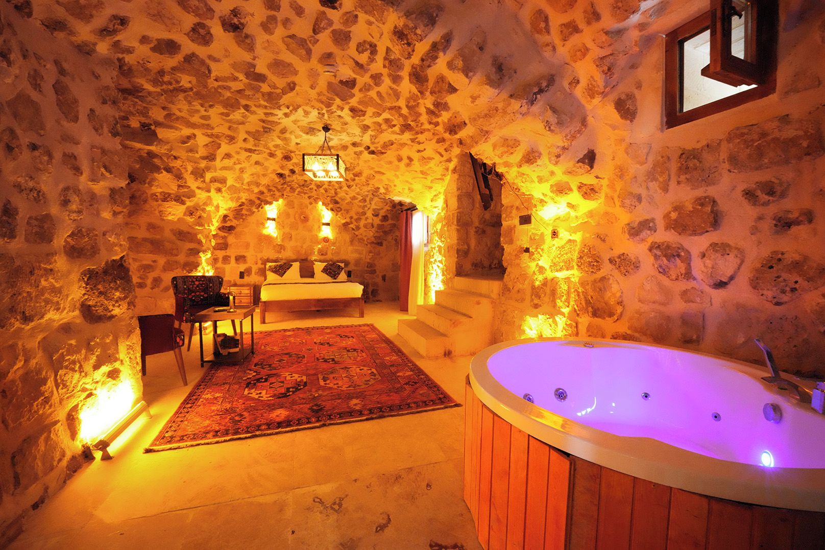 A stone-walled room with a wooden bathtub, a bed, and a small table with chairs.