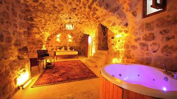 A stone-walled room with a wooden bathtub, a bed, and a small table with chairs.
