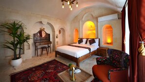 A bedroom with a bed, a desk, a chair, a potted plant, and a red curtain. - NUHARA OTEL (Mardin)