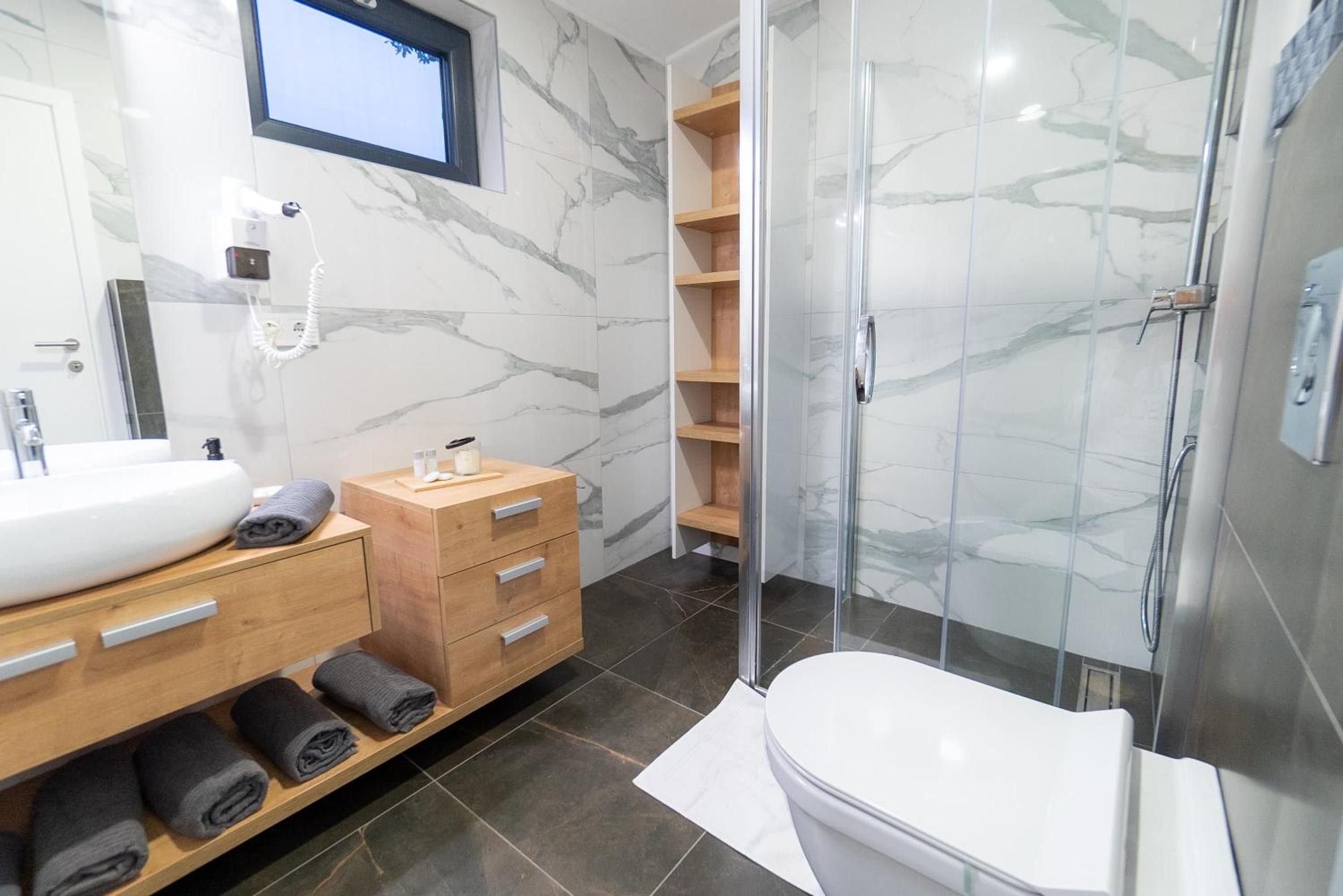 Une salle de bain moderne avec un mur en marbre, un lavabo blanc, un meuble-lavabo en bois, une cabine de douche en verre et des toilettes.