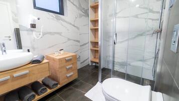 Une salle de bain moderne avec un mur en marbre, un lavabo blanc, un meuble-lavabo en bois, une cabine de douche en verre et des toilettes.