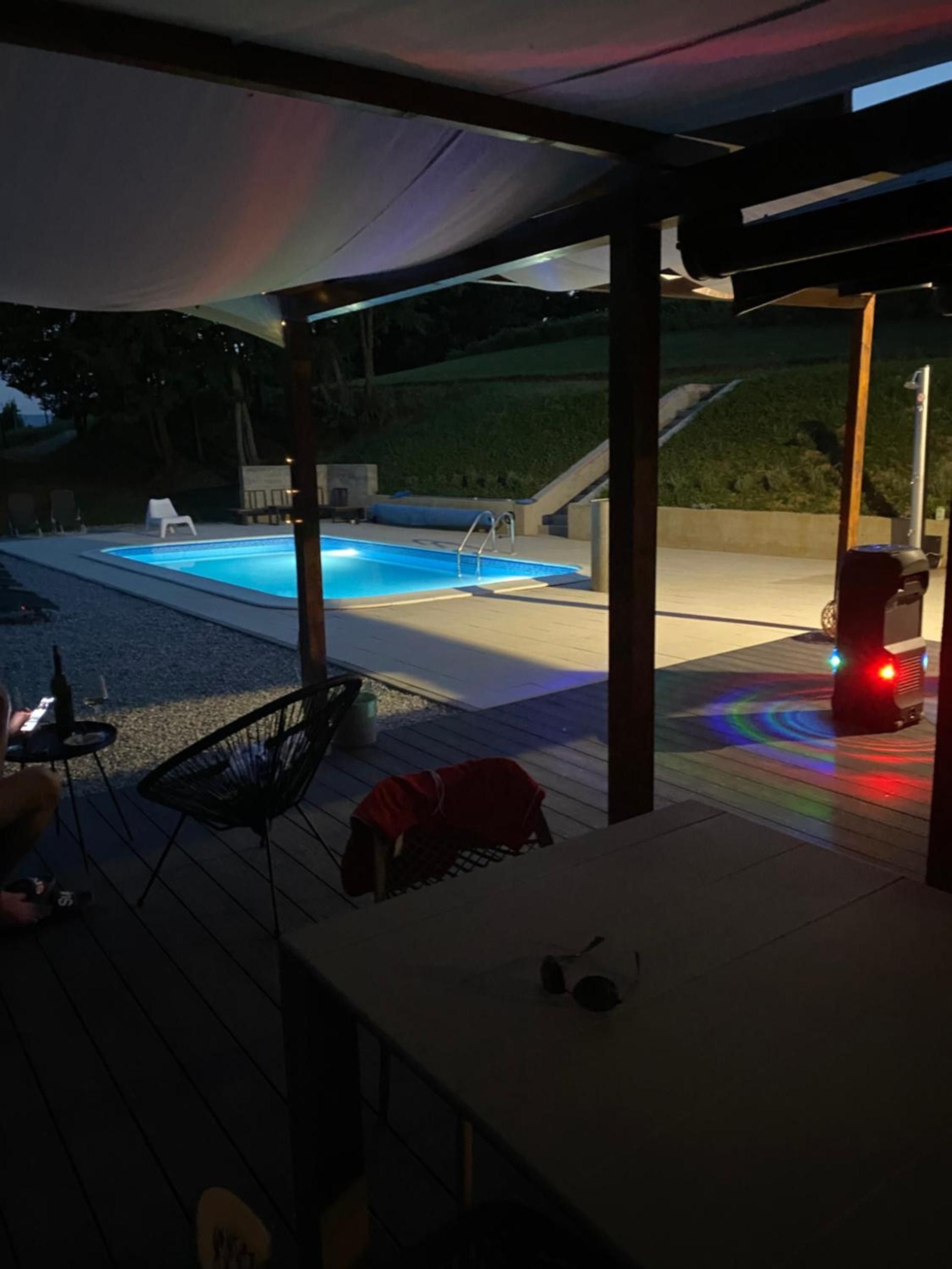 An outdoor pool area with a covered patio, a chair, and a red object on the deck.