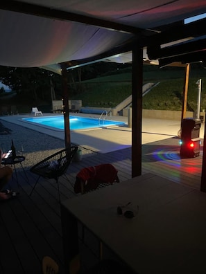 An outdoor pool area with a covered patio, a chair, and a red object on the deck.